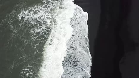 Una-Toma-Aérea-De-Las-Olas-De-La-Playa-De-Reynisfjara-Rompiendo-En-Islandia