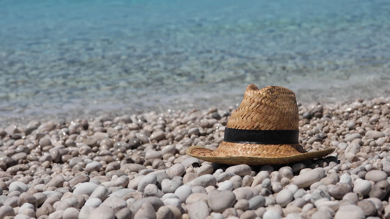sombrero de paja en la playa de guijarros con fondo de agua de mar cristalina, concepto de vacaciones