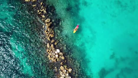 Vista-Aérea-De-Una-Pareja-En-Un-Kayak-En-Las-Aguas-De-La-Playa-Mambo-Con-Un-Rompeolas-A-Un-Lado,-Curacao,-Isla-Caribeña-Holandesa