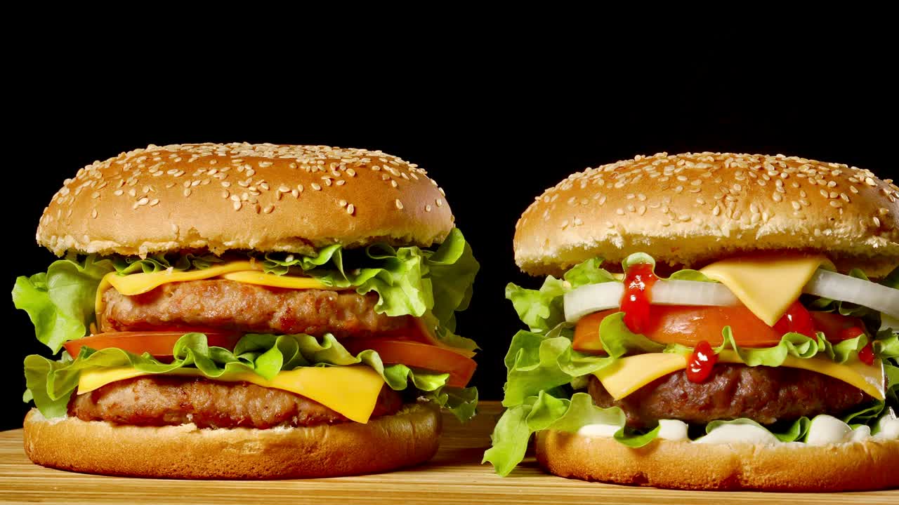 primer plano de dos hamburguesas apetitosas con panes de sésamo girando sobre un fondo negro, de comida rápida en bucle sin costuras