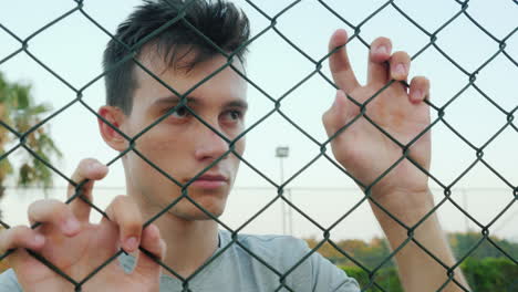 depressed teenager looks over the fence mesh