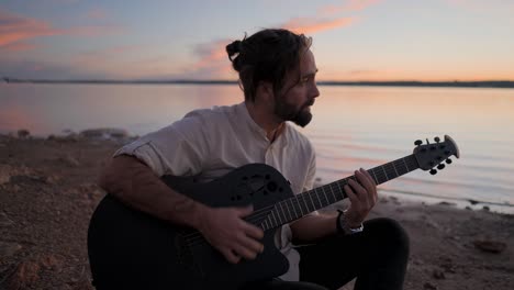 Man playing guitar at sunset by the lake