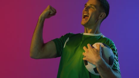 feliz jugador de fútbol masculino caucásico con fútbol sobre iluminación rosa neón