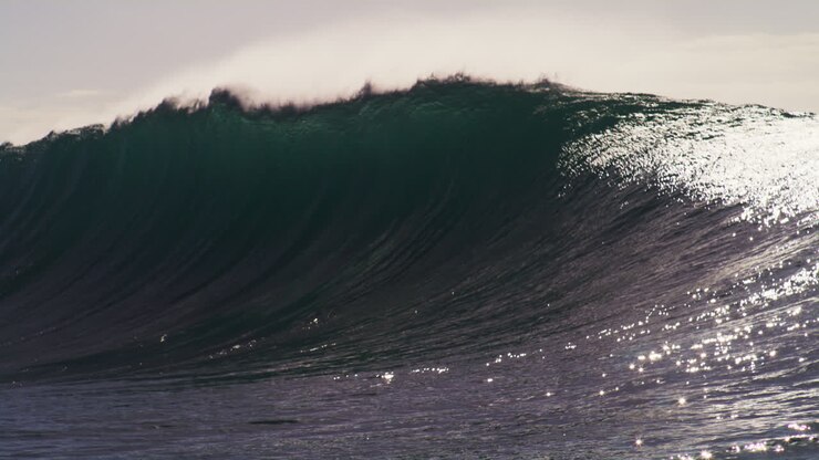 Glistening sunlight across big wave crashing down on surface of ocean