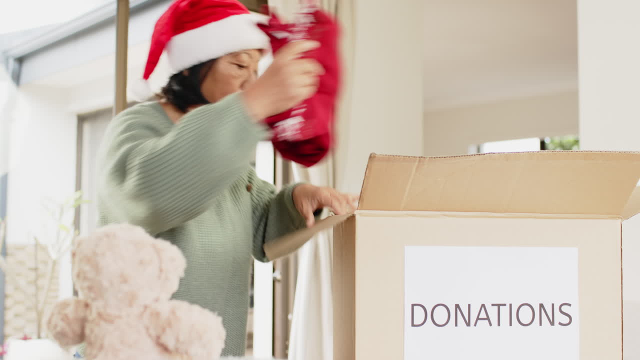 Elderly woman in Santa hat donating teddy bear at home during Christmas
