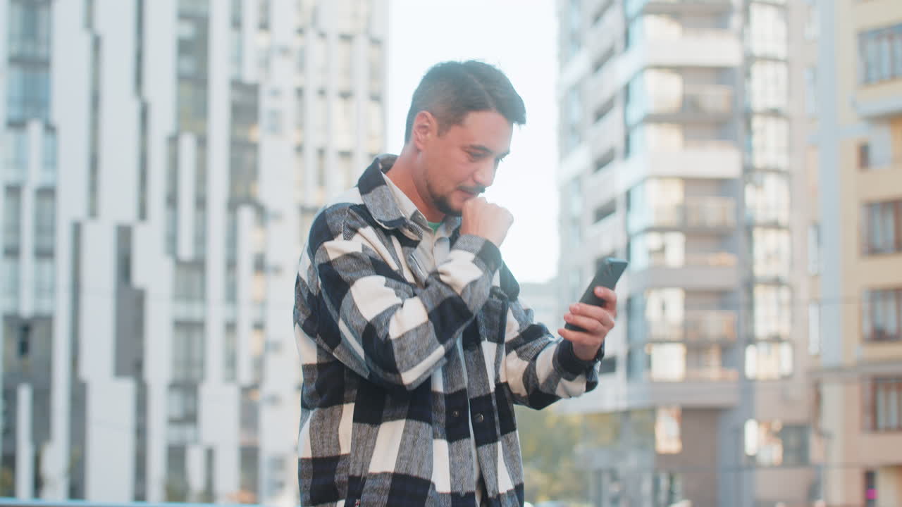 Happy young man using smartphone celebrating victory win good message news on downtown city street