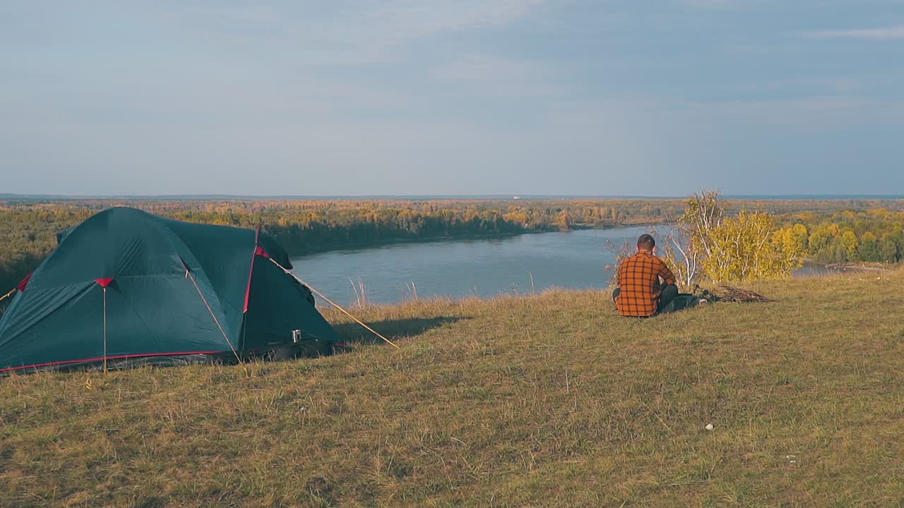 한 남자가 아침 느린 움직임으로 강변에 있는 불꽃에 앉아 있습니다.