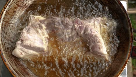 tender pork belly is being cooked in hot bubbling oil in top down view