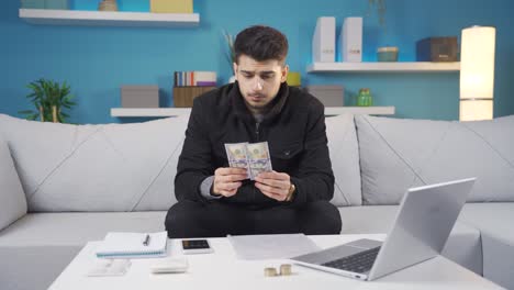 unhappy young man looking at high priced electricity and gas heating bills in cold room at home.