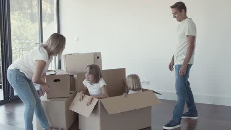 parents opening big cartoon box with cheerful daughters inside