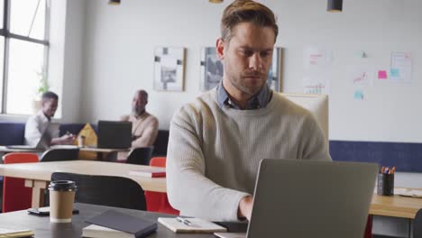 happy caucasian businessman sitting at table and using laptop at office