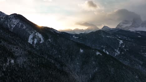 drone aerial view of mountains with snow in winter, dramatic light with clouds in the sky during sunset