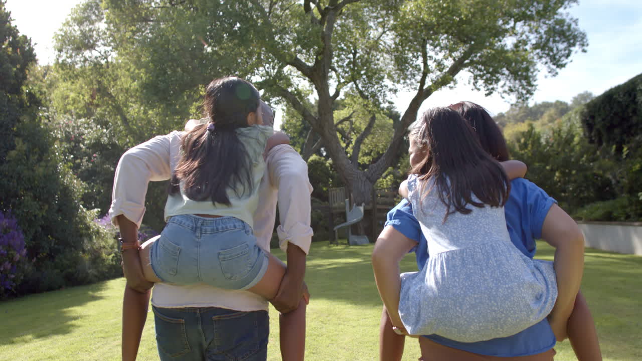Parents giving piggyback rides to children, enjoying family time outdoors