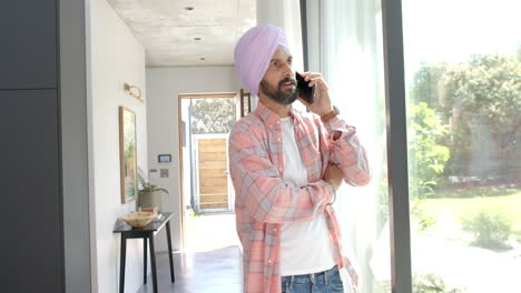 talking on smartphone, man in turban standing by window at home