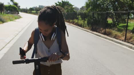 mujer afroamericana en scooter usando un teléfono inteligente y sonriendo