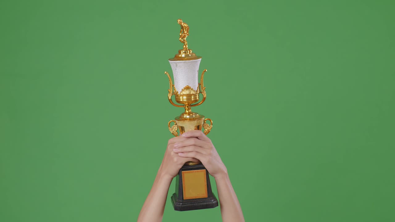한 남자의 손이 트로피를 들고 있다. 녹색 화면 배경