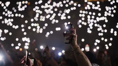 spectators crowd arms up holding luminous phones during music concert show, arena stands in background with bokeh defocused lights in dark, romantic atmosphere