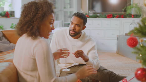 loving couple drinking champagne and opening gifts around christmas tree at home