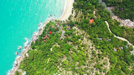 peaceful tropical island shoreline with rocks and sandy beach, lush vegetation and resort villas with beautiful ocean view in thailand