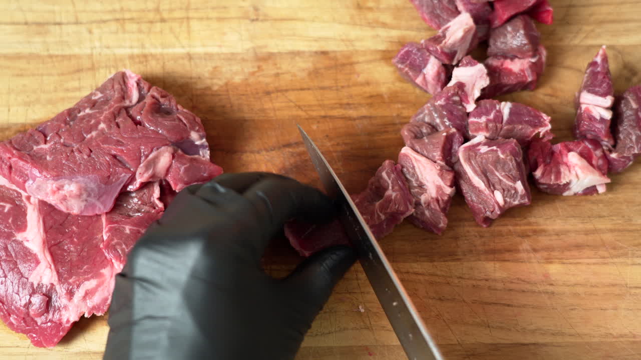 Chef is dicing the most delicious fresh chuck of beef, using black gloves and sharp chef knife