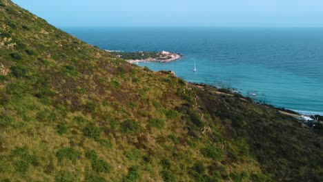 Escénica-Cerdeña-Azul-Turquesa-Claro-Y-Aguas-Tranquilas-En-Una-Bahía-De-La-Costa-De-La-Playa-De-Arena-Natural-En-Italia-Con-Sol-Y-Un-Velero