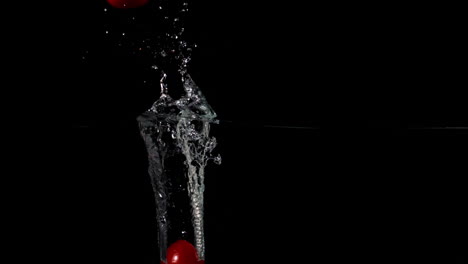 Tomate-Cherry-Cayendo-Al-Agua-Sobre-Fondo-Negro