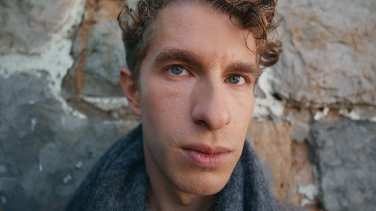 Fashion model posing stoned wall standing alone closeup. Man looking camera