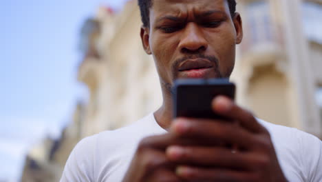 frustrated afro guy using mobile on street. man texting message in smartphone