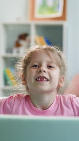 cute blonde girl plays with colorful plastic balls. child with toothless smile sits in azure dry pool in light apartment on blurred background