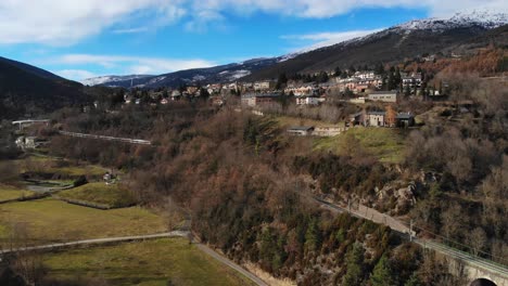 antena: tren de pasajeros que atraviesa un valle en un paisaje montañoso y picos nevados en el fondo