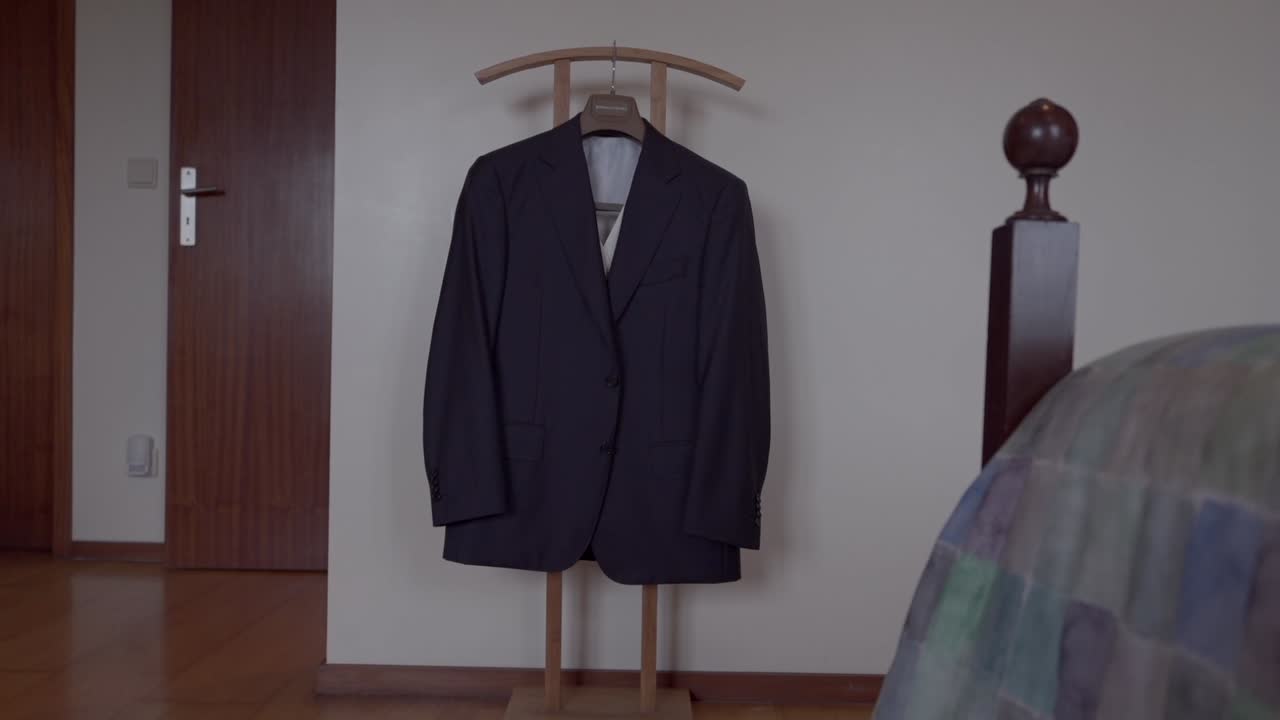 Black suit neatly hung on a wooden valet stand in a minimalist bedroom setting