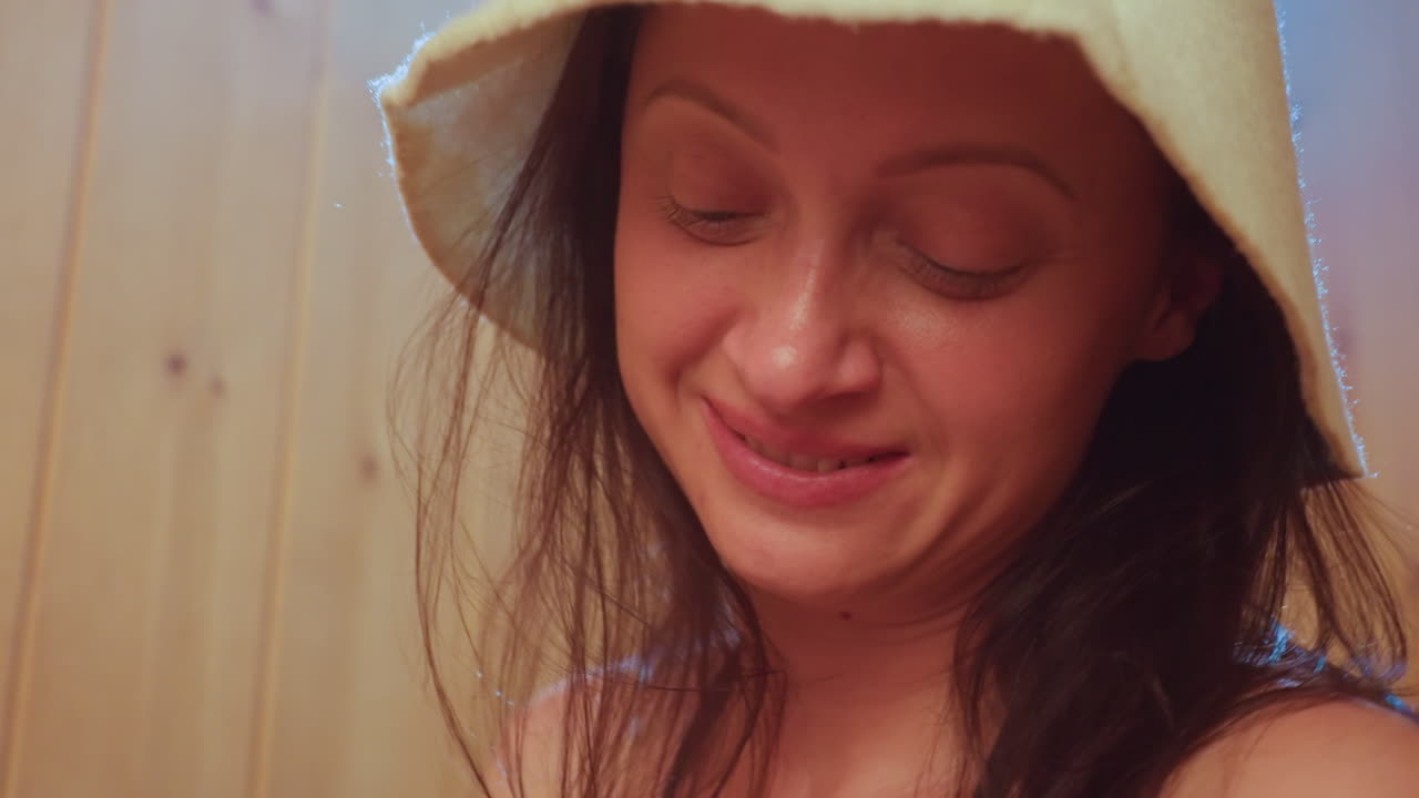close up portrait of elegant woman wearing sauna hat looking up with warm smile inside wooden sauna cabin capturing serene wellness moment and calm relaxation mood