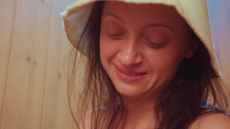 close up portrait of elegant woman wearing sauna hat looking up with warm smile inside wooden sauna cabin capturing serene wellness moment and calm relaxation mood