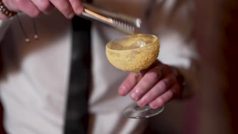 Bartender-Puts-Ice-Cubes-Into-Cocktail-Glass-With-Tongs-Close-Up