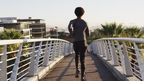 rear view of fit african american man exercising outdoors in city, running on footbridge