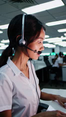 young woman wearing headset, concentrating while working on computer in busy call center environment, providing customer support with professional efficiency