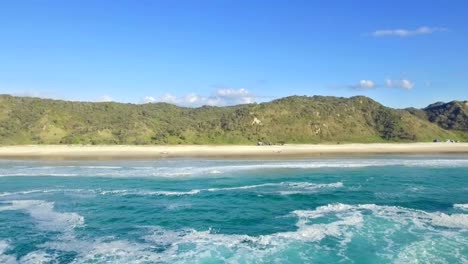 Sanfter-Drohnenschuss,-Der-über-Die-Schaumigen-Wellen-Und-Zurück-Zum-Ufer-Der-Herrlichen-Fraser-Insel-Kìgari-Fliegt,-Während-Ein-Einsames-Allradauto-Den-Strand-Hinauffährt