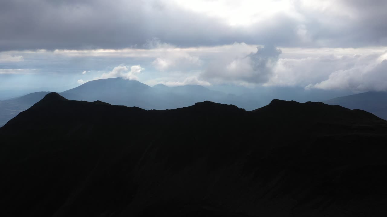Sweeping aerial shot passes over Cnicht mountain in Wales under dramatic skies, curving to reveal distant coastline. Rugged terrain and moody lighting create a cinematic natural landscape.