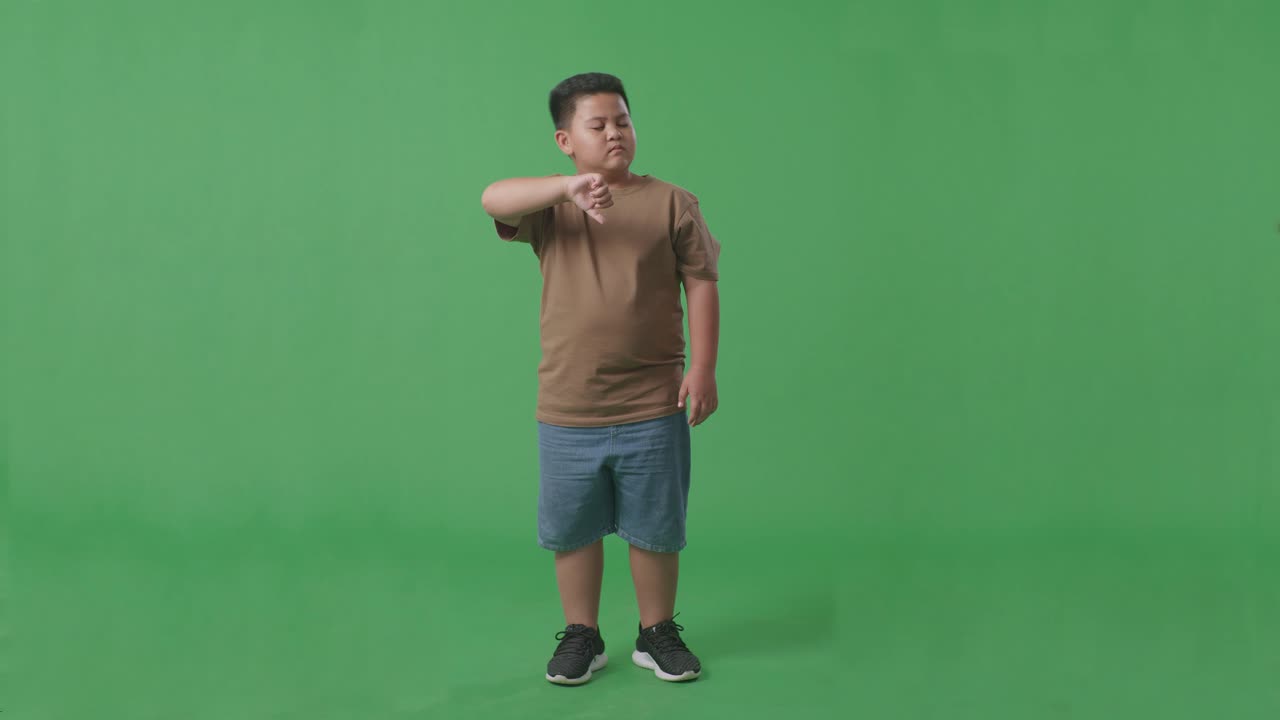 녹색 스크린 스튜디오에 서 있는 동안 엄지손가락을 내려놓은 아시아 소년의 몸이 가득 차 있습니다.