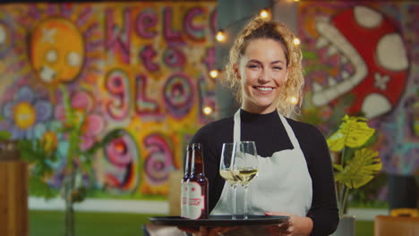 Portrait-Of-Smiling-Female-Server-Holding-Tray-Of-Drinks-In-Cool-Bar-Or-Club