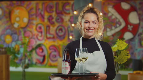 retrato de una camarera sonriente sosteniendo una bandeja de bebidas en un bar o club fresco