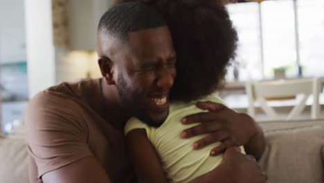 african american daughter and her father smiling and hugging on couch