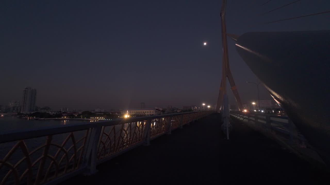 하늘에 달이 보이고 거리를 조명하는 거리 조명과 함께 다리 위의 황혼 장면, 현대적인 건축물과 멀리 떨어진 스카이 라인이 조용하고 평화로운 환경을 만니다.