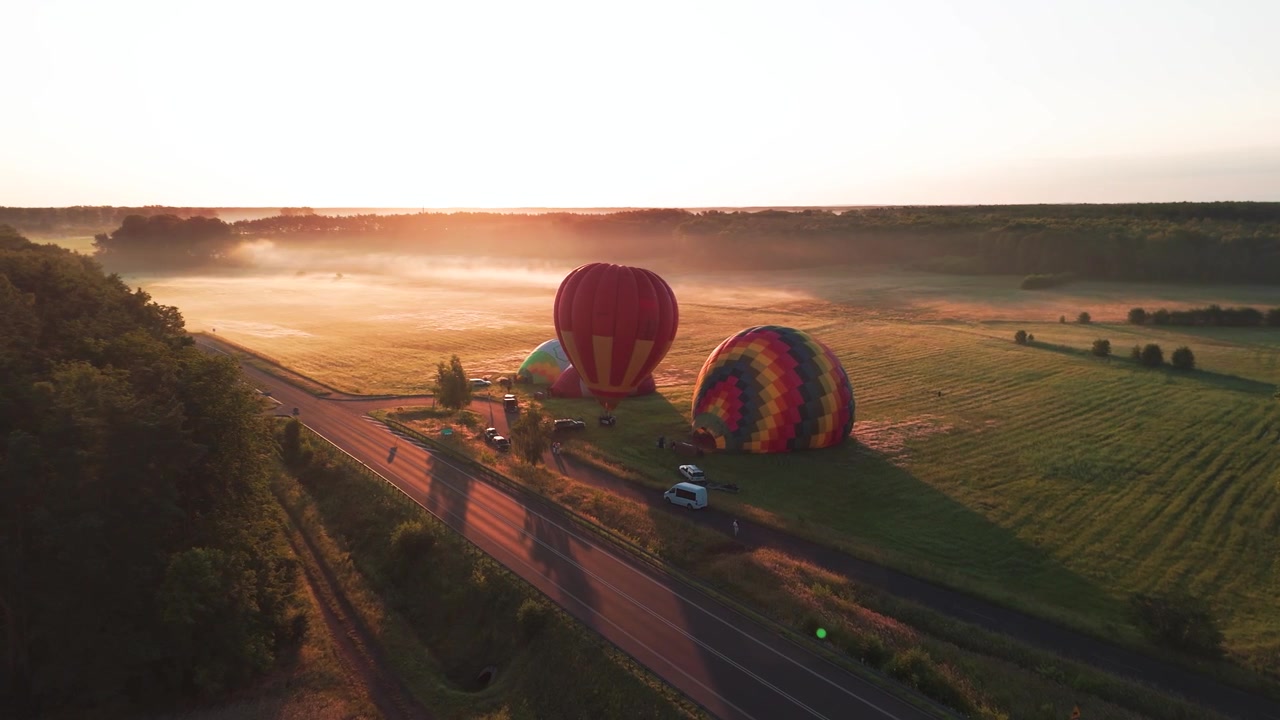 Ripresa aerea cinematografica di mongolfiere colorate che si gonfiano in un campo rurale durante un'alba nebbiosa. Ottimo per contenuti di viaggio, avventura e benessere