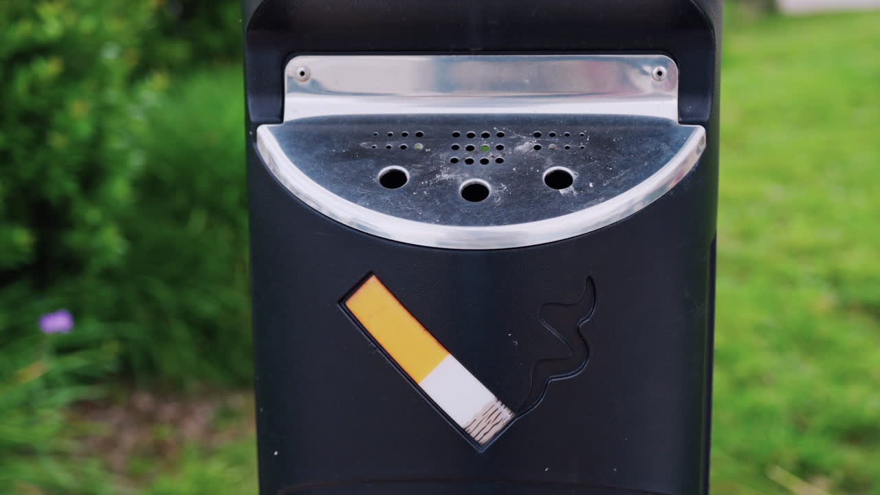 Close up of a cigarette trash can with a blurred garden on the background