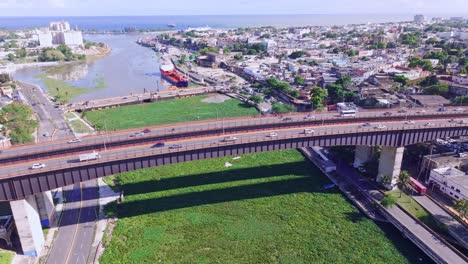 Car-traffic-over-Puente-Ramon-Matias-Mella-bridge-across-the-Rio-Ozama-clogged-with-invasive-water-hyacinth,-aerial-view