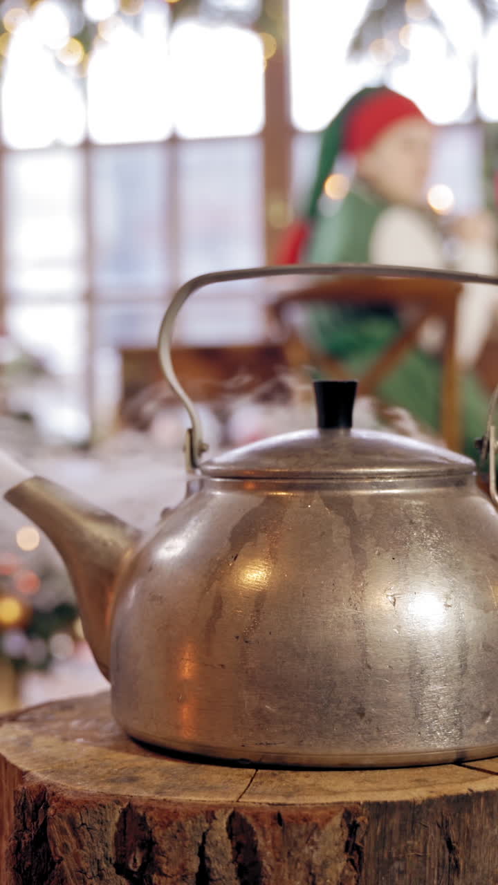 Boiling kettle in the room on blurred Christmas background. Hot kettle with boiled water and white steam on wooden log. Vertical video
