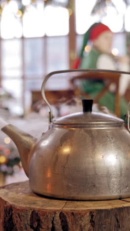 boiling kettle in the room on blurred christmas background. hot kettle with boiled water and white steam on wooden log. vertical video