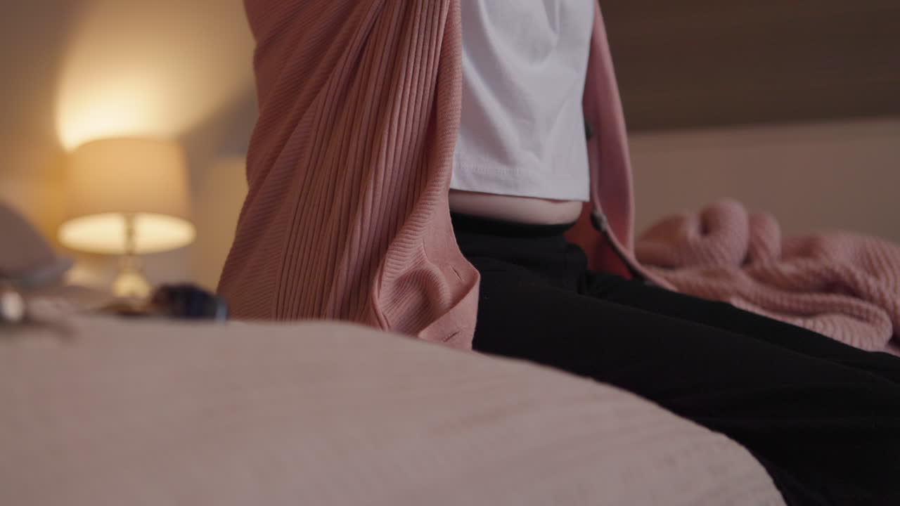 Woman in pink cardigan sitting on bed