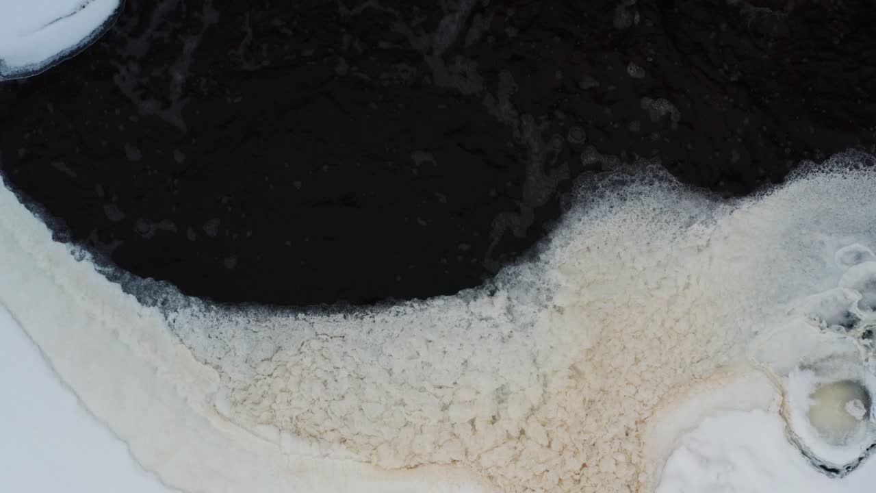 얼어붙은 연못의 어두운 물줄기가 해안 근처에 노란색 거품을 형성합니다.